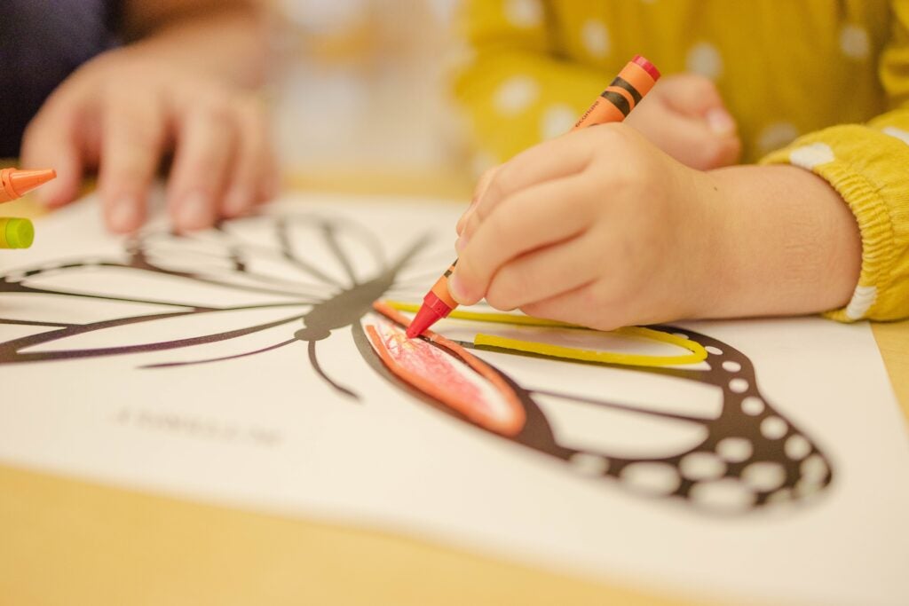 Child coloring in a butterfly with an orange crayon
